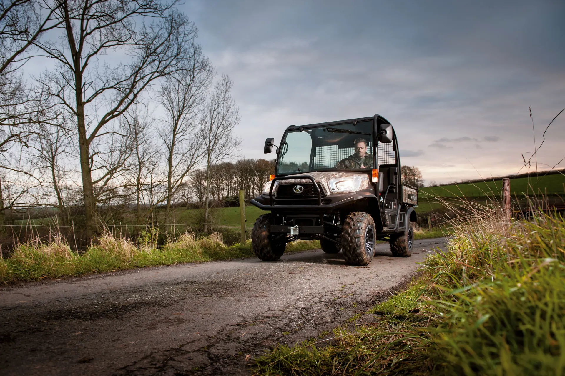 Kubota RTV X1110 (C) u kamuflažnoj boji Realtree s kabinom vozi seoskim putem uz polje