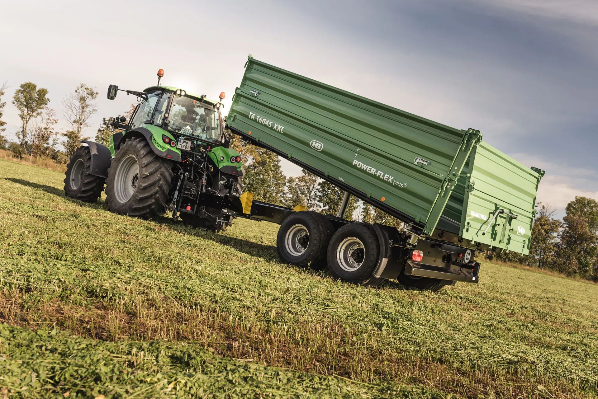 Brantner TA 16045 XXL tandem kiper s podignutim sandukom, prikopčan na zeleni traktor na livadi