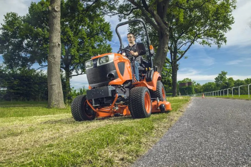 Kubota BX s ROPS okvirom i srednjim kosištem kosi travu uz put, pogled odozdo sprijeda