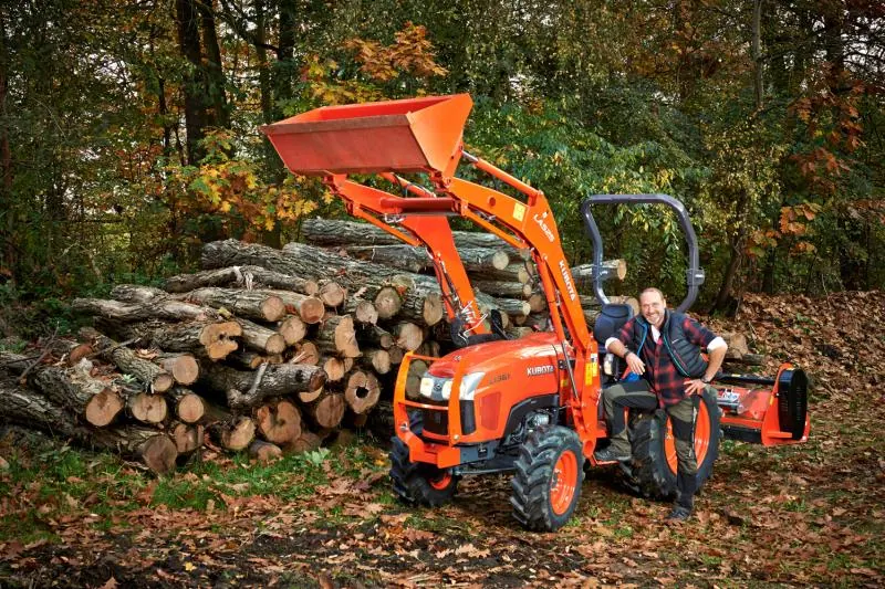 Traktor Kubota L1 s prednjim utovarivačem i malčerom uz složene trupce u šumi