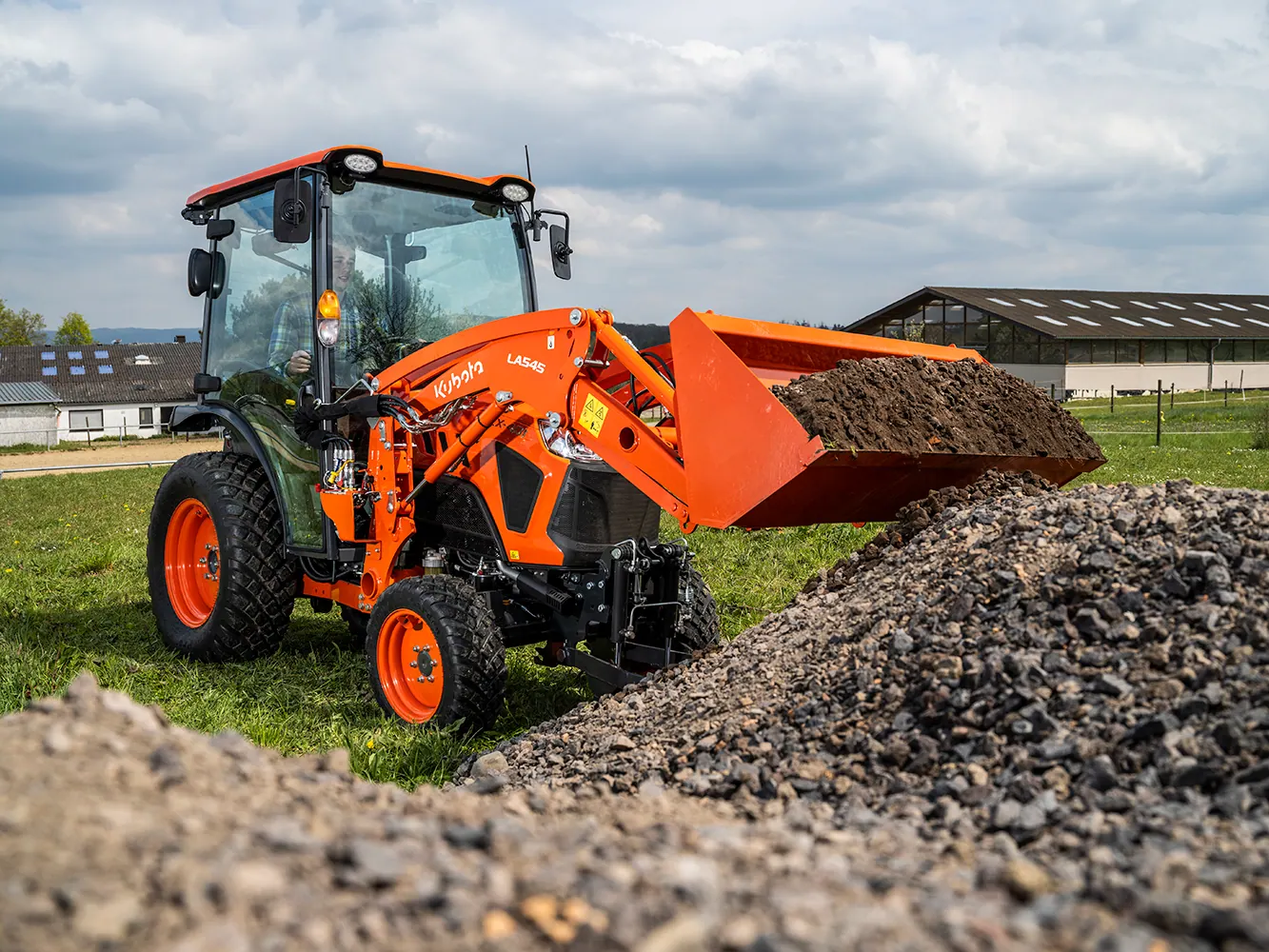 Kubota LX s kabinom i prednjim utovarivačem podiže zemlju iznad hrpe šljunka