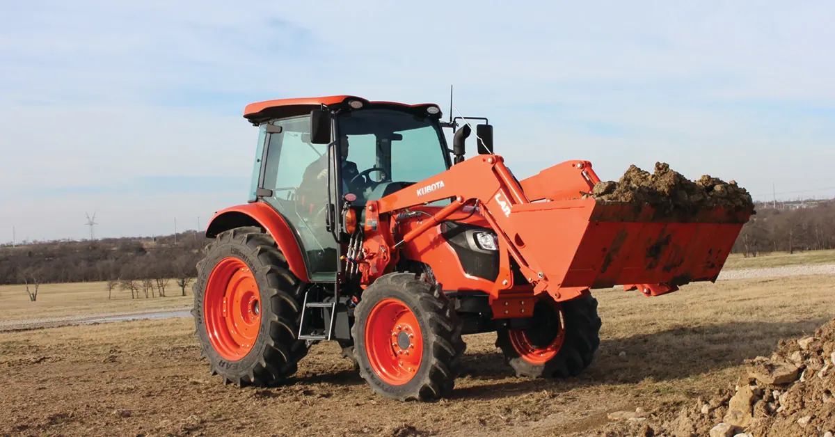 Kubota M4 s kabinom i čeonim utovarivačem prevozi zemlju u žlici preko oranice
