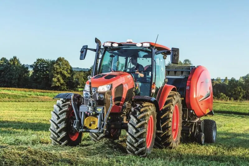 Kubota M5002 s kabinom i prednjim podizačem vuče prešu za okrugle bale po pokošenoj livadi